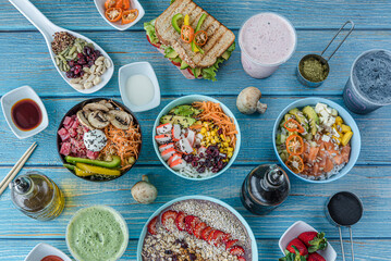 Flat-lay of various kinds of healthy food in plates and bowls on blue wood, top view.