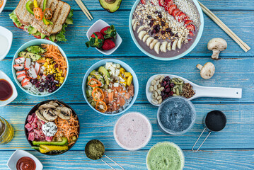 Flat-lay of various kinds of healthy food in plates and bowls on blue wood, top view.