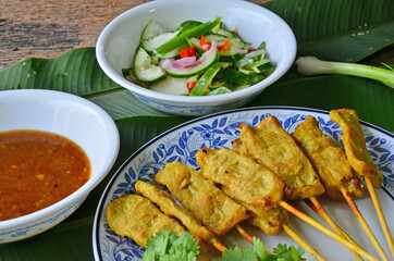 Pork satay with peanut sauce and side dish on green banana leaf floor