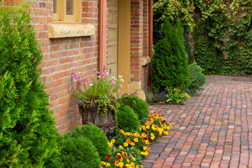 Full frame texture background of a 19th century red clay brick wall with charming weathering from age, with view of a window and attractive foundation plants