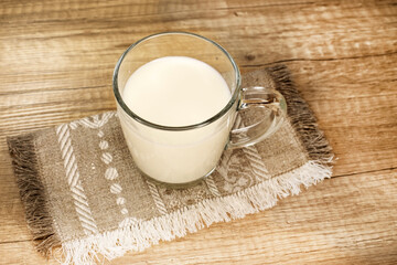 A transparent cup with milk stands on a material with a pattern. Wooden table. The concept of health and Breakfast