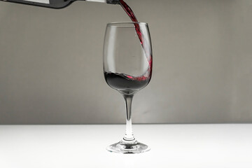 Red wine is poured from a bottle into a glass on a blurred background, close-up.