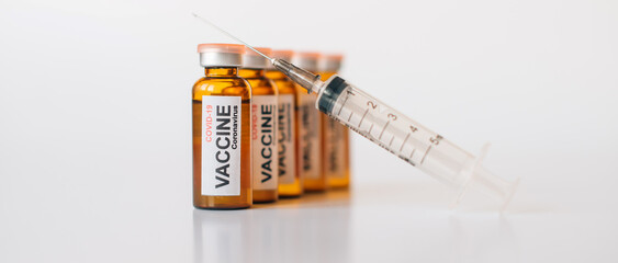 Tined glass vaccine vials with label and medical syringe with needle up on white background. Banner...