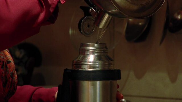 Woman pouring Hot Water into a Thermos in her Kitchen. Close Up. 