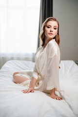 beautiful woman with makeup, long hair sits in white robe on bed