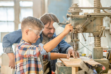Man teaches the boy to work on the drilling machine