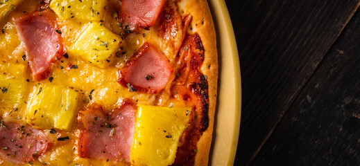 Just baked hawaiian pizza with freshly chopped pineapple and ham on the rustic wooden background....