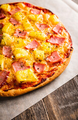 Just baked hawaiian pizza with freshly chopped pineapple and ham on the rustic wooden background. Selective focus.
