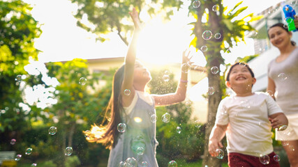 Happy Asian family relationship at home. Mother with little daughter and son playing soap bubbles in backyard garden. Joyful parent with two child kids relax and having fun weekend activities together