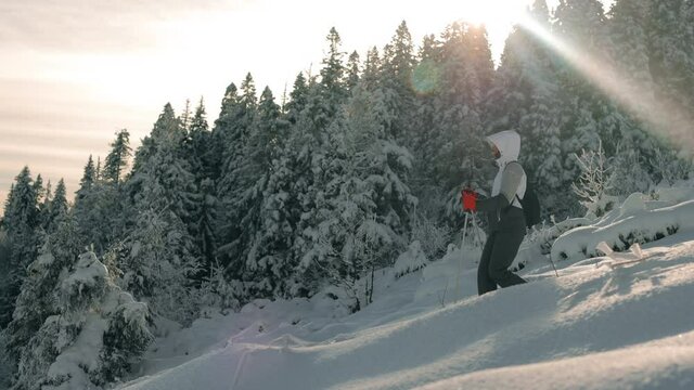 A young woman is descending from a snow-covered mountain. She is rising with the help of trekking poles. Snow-covered forest in the background. Mount Pikui. 4K.
