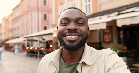 POV of cheerful African American young handsome man talking to camera while videochatting outdoors. Happy guy speaking and having videochat at street in town. Male communicating online.