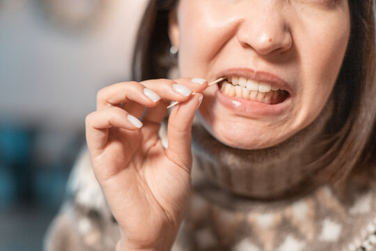 Asian woman has a toothache after a big meal and she pulls out the remains of food from the cavity in her teeth with a toothpick. The concept of dental health and cleaning