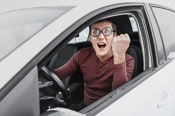 Funny and ridiculous nerd driver in eyeglasses shouting to the camera and showing his fist inside a...