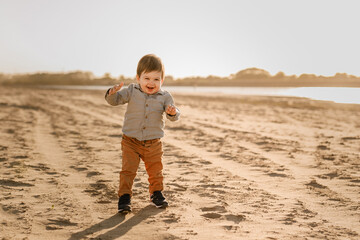 A one-year-old boy learns to walk in the sand by the river