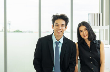 Concept of partnership in business. a man in a suit and a woman in a black dress standing in the office looking at the camera with confident smiles at the success of their partnership