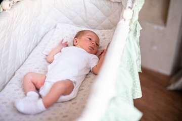 Fototapeta na wymiar Newborn baby boy in bed. New born child in white bodykit lying in light cradle. Children sleep. Bedding for kids. Infant napping in bed. Healthy little kid shortly after birth