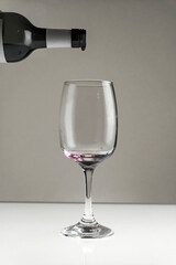 Red wine is poured from a bottle into a glass on a blurred background, close-up.