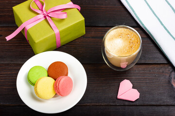 Macaroni macaroon on white plate, holiday gift, glass of latte and romantic heart shaped note. Romantic Flat Lay