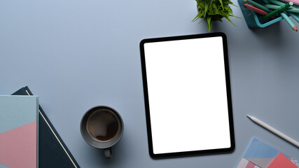 Top view of creative designer or stylish workspace with mock up digital tablet, notebook, coffee cup and plant on gray table.