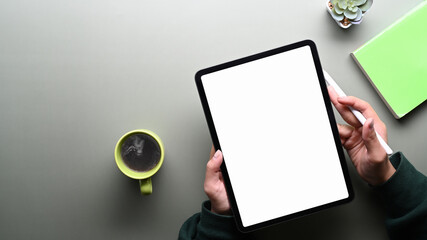 Top view of young woman in green sweater holding stylus pen and digital tablet with blank screen on gray table.