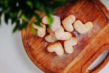 Heart-shaped cookies on round wooden cutting board. Saint Valentine's cookies in shape of heart on white background. Green leaveas and pastry. Spring freshness.