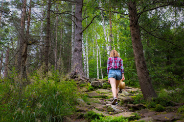 Naklejka na ściany i meble Hipster girl in the mountains. Stylish woman in straw hat and checkered shirt in forest. Wanderlust concept. Travelling and hiking in summer. mysterious wood. Beautiful nature.