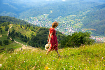 Beautiful girl the mountains. Woman in linen dress and straw hat travelling. Amazing summer nature around. Harmony and wanderlust concept. Rustic natural style. Wind blowing for dynamic photo.
