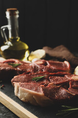 Board with raw steak meat, herbs and spices on black smokey background