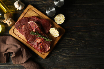 Spices, oil and board with raw steak meat on wooden background