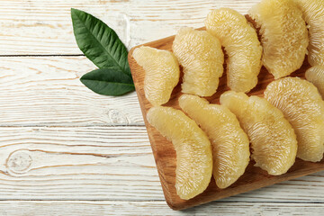 Board with pomelo slices and leaves on wooden background
