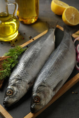 Board with herring fish and spices, and oil on dark wooden background
