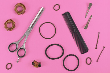 Hair styling concept with elastic hair ties, hair pins, comb and thinning shears on pink background