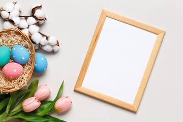 Happy easter. Multicolored eggs in a basket, tulips, a cotton branch and a frame on a gray background. Flat lay greeting card copy space.