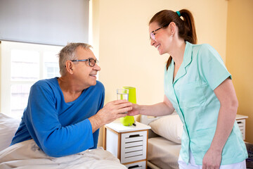 Loving nurse handing glass of water to her nursing occupant in a elder peoples home