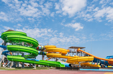 Obraz na płótnie Canvas Water park, bright multi-colored slides with a pool. A water park without people on a summer day with a beautiful, cloudy blue sky