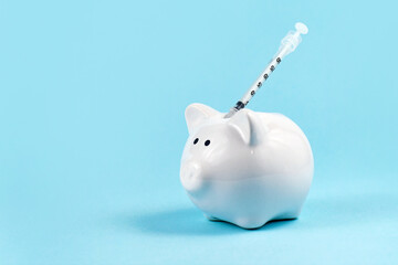 Cash infusion or Corona virus vaccine expenses concept with white piggy bank and syringe on blue...