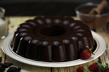 plate of chocolate pudding with strawberries and chocolate slices on the background of a small bottle of milk and a small bowl of cocoa powder on a wooden table