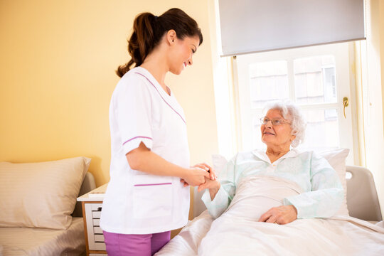 Nursing home doctor holding a hand of a senior woman patient occupant while she is lying
