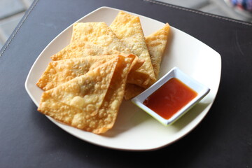 fried dumplings in a stack with a bowl of chili sauce