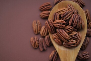 Pecan nut  in wooden spoon on bright brown background.Healthy fats.Heap shelled Pecans nut closeup. Ingredient of the keto diet.Tasty raw organic food and healthy snack