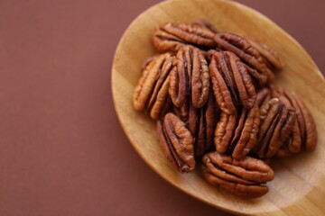 Pecan nut close-up in wooden spoon on bright brown background.Healthy fats.Heap shelled Pecans nut. Ingredient of the keto diet.Tasty raw organic food and healthy snack