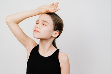 A teenage girl in a black T-shirt holds her hand on her forehead against a white background. headaches or high body temperature. illness or fatigue. copy space