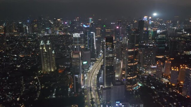 Descending aerial pedestal shot of night time highway traffic through busy modern city center in Jakarta