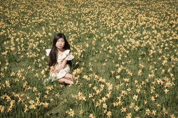 Girl sitting outside in field of yellow daffodils flowers