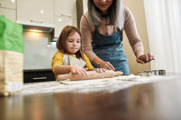 Little girl rolling dough under grandmother supervision