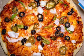 Top view of a cheesy vegetarian pizza topped with black olives, green bell peppers, onions, and jalapeño in a takeout box