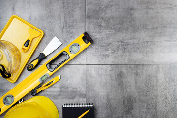 Contractor concept. Tool kit of the contractor: yellow hardhat, libella, hand saw on the gray tiles...