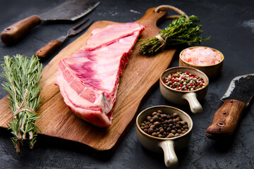 Raw lamb breast and flap on wooden cutting board with herbs and seasoning