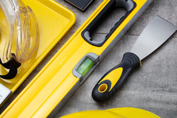 Contractor concept. Tool kit of the contractor: yellow hardhat, libella, hand saw on the gray tiles background.