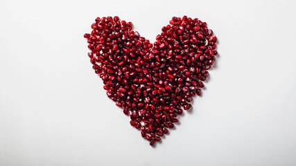 Obraz na płótnie Canvas Heart shape pomegranate seeds on white background. Valentines helthy love concept.